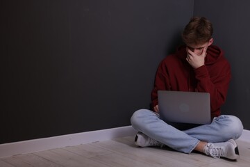Cyber bullying. Upset teenage boy with laptop on floor indoors. Space for text