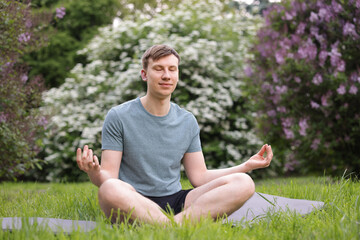 Young man practicing yoga on mat in park