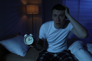 Frustrated man with alarm clock suffering from insomnia on bed indoors