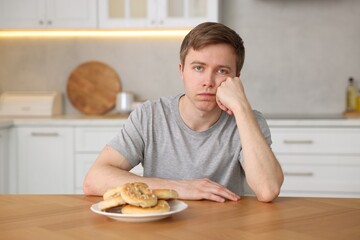 Gluten free diet. Sad woman with pretzels at wooden table in kitchen