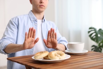 Gluten free diet. Man refusing from pastries at wooden table indoors, closeup