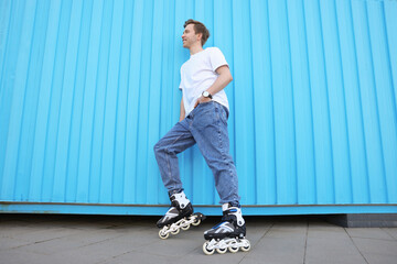 Happy young man with roller skates near light blue wall outdoors, low angle view