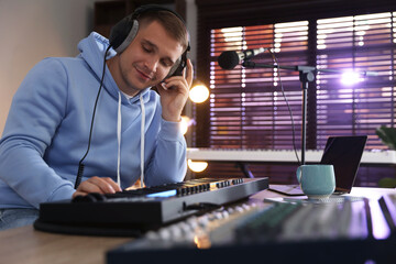 Man in headphones working with MIDI keyboard at table in home studio, low angle view
