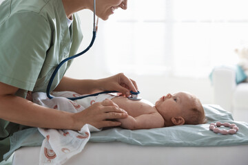 Pediatrician examining baby with stethoscope at table in clinic, closeup