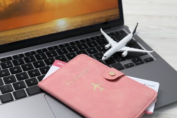 Passport, flight ticket, plane model and laptop on white wooden table, closeup