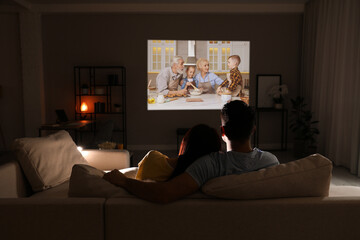 Couple watching movie using video projector on sofa at night