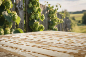 Empty wooden table with copy space in front of green hops growing on a fence in sunny rural setting.