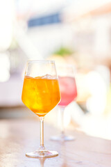 Glasses of pink and yellow alcoholic drink Aperol Spritz with ice on table on warm day. Celebration with glasses of refreshing fruity soft drink