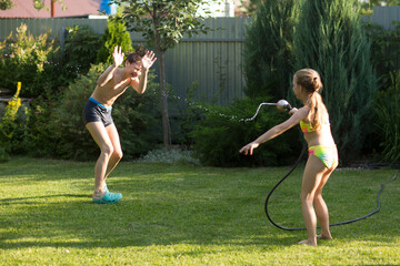 Happy children brother and sister playing in the garden hose and having fun with spray of water in...