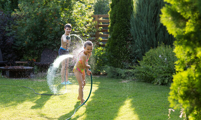 Happy children brother and sister playing in the garden hose and having fun with spray of water in...