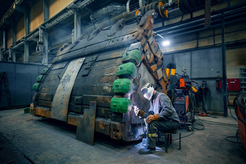 Welder repairs excavator truck bucket in repair garage. Fix Service of industry mining factory.
