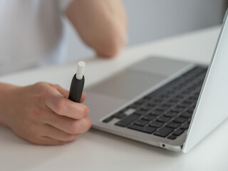 A woman smokes an electronic cigarette while working on a laptop. Tobacco heating system.