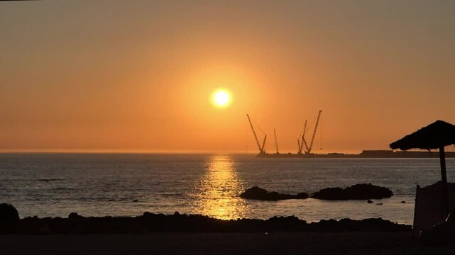 Sunset at Homem do Leme beach in Porto, Portugal, on July 8, 2025, showing silhouetted beach umbrellas and cranes against a golden sky, capturing a peaceful holiday evening by the Atlantic Ocean.