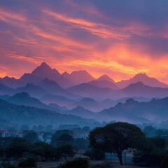 Fototapeta premium The mountains are covered in a misty blue haze, and the sun is setting behind them. The sky is a mix of orange and pink hues, creating a serene and peaceful atmosphere