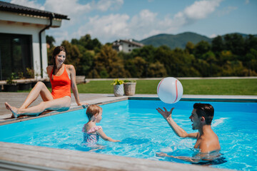 Young family with small daughter in swimming pool outdoors in backyard garden.