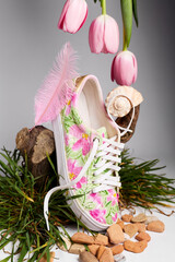 Floral sneaker with pink tulips, feather, seashell, and grass on studio background