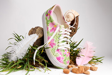 Colorful floral sneaker with seashells, feathers, and grass on white studio background