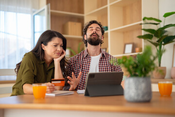 Frustrated couple managing finances at home, discussing with stress and concern.
