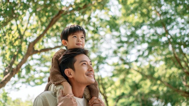 Father giving son ride on back in park. Portrait of happy father giving son piggyback ride on his shoulders and looking up. Cute boy with dad playing outdoor., no logos, no brands
