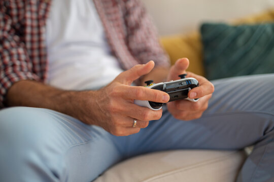 Close-up of man's hands holding a video game controller while sitting on a couch.
