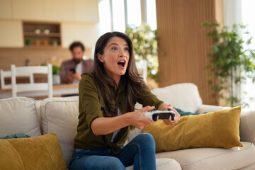Obraz premium Focused young woman with surprised expression playing video games with controller at home. 