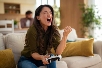 Energetic young woman cheering and shouting while playing video games at home.
