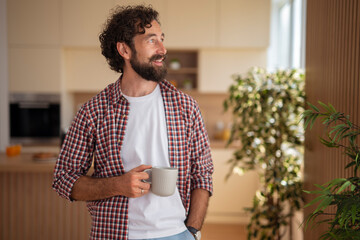 Young man enjoying morning coffee while standing in bright kitchen at home.
