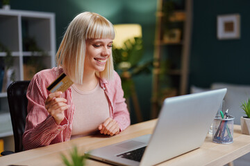Happy woman making online payment using laptop and credit card at home