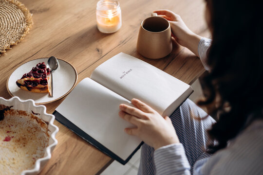 Close-up of a woman reading her Bible while having breakfast in a cozy kitchen.
