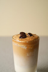 A delicious iced coffee drink features a layer of frothy whipped coffee foam topped with whole coffee beans in a clear glass. The beverage shows a smooth gradient of colors, inviting enjoyment