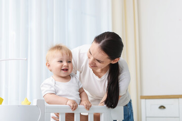 Mother playing with her cute baby in crib at home