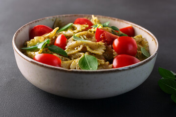 Aromatic homemade vegan farfalle with green pesto sauce, cherry tomatoes, basil leaves and homemade spcy olive oil close up Healthy vegan food concept.