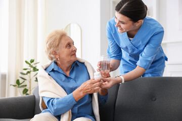 Nurse giving glass of water and pills to senior woman indoors. Home health care service