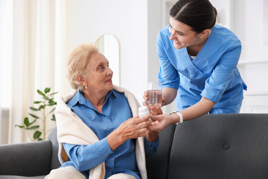 Nurse giving glass of water and pills to senior woman indoors. Home health care service - Powered by Adobe