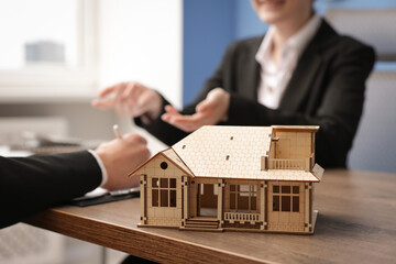 Real estate agent working with client at desk in office, focus on house model