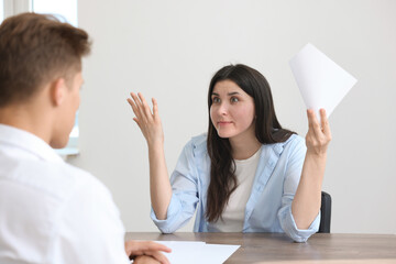Young woman complaining to man at wooden table indoors
