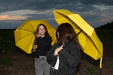 Two young attractive women with yellow umbrellas against stormy sky in the evening	