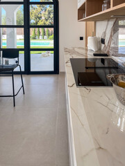 Modern kitchen interior featuring sleek marble countertop, stylish black chair, and large windows...