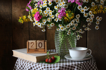 Bouquet of wildflowers, teacup, book and wooden calendar showing july 20th