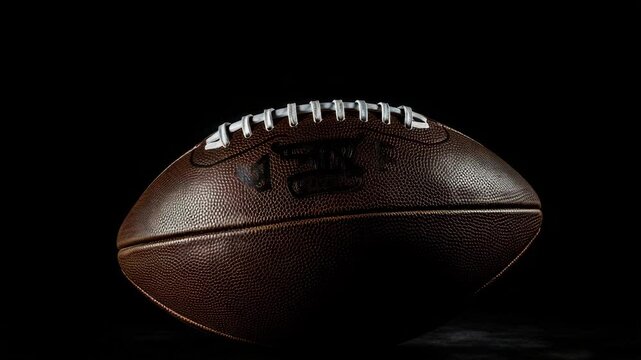 A close-up shot of an American football placed against a stark black background, emphasizing the ball&rsquo;s textured surface, stitching, and iconic shape&mdash;creating a dramatic, high-contrast vis 4K.