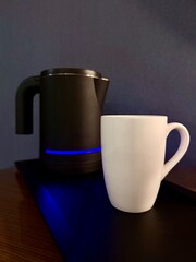 A modern black electric kettle next to a white ceramic mug on a kitchen counter. Minimalist home...