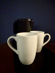 A modern black electric kettle and two white ceramic mugs on a kitchen counter. Minimalist home...