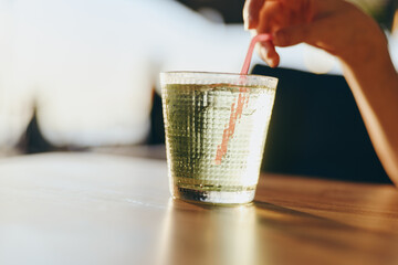 glass of sparkling water with hand stirring pink straw on wooden table in bright natural light,...