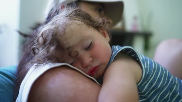 Toddler sleeping soundly on mother&rsquo;s shoulder, flushed cheeks and peaceful face resting in tender embrace indoors during daytime