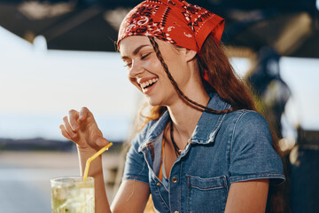 Lifestyle woman in modern boho-western denim street style enjoys refreshing drink outdoors with...