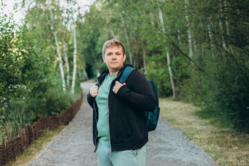 Young happy smiling 30s man with backpack walk in green city park outdoors on nature. Lifestyle...