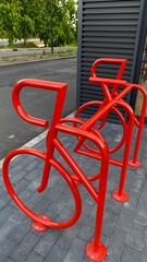 Modern red bike rack shaped like a bicycle in urban setting near contemporary building