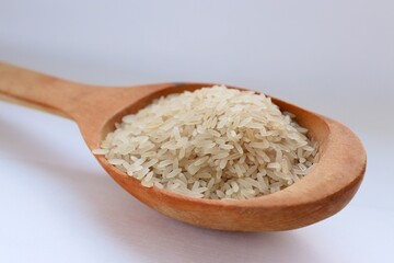 White rice in a wooden spoon on white background, close-up — concept of natural nutrition, visual purity and culinary simplicity for healthy lifestyle