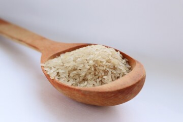 White rice in a wooden spoon on white background, close-up — concept of natural nutrition, visual...