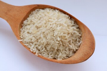 White rice in a wooden spoon on white background, close-up — concept of natural nutrition, visual purity and culinary simplicity for healthy lifestyle